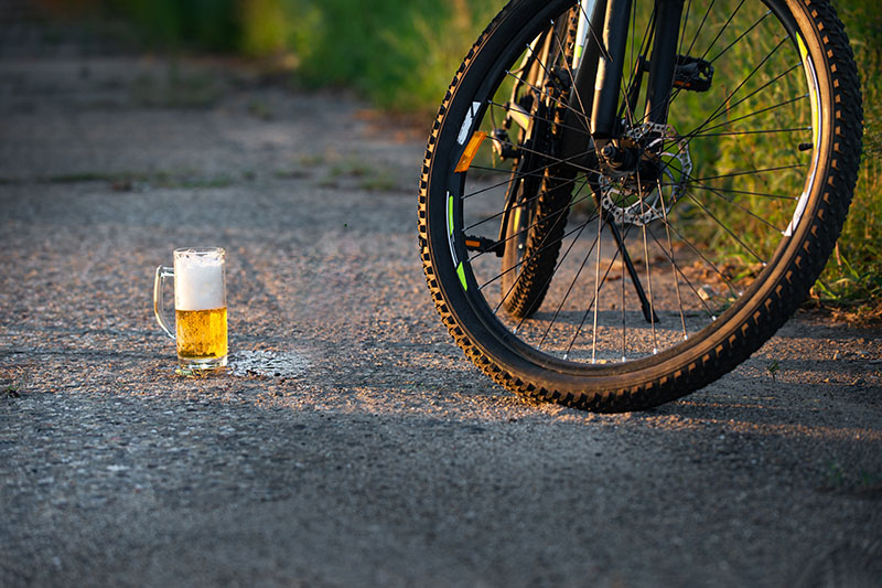 Närbild på ett cykelhjul som står vid sidan av vägen med ett glas skummande öl bredvid, foto.