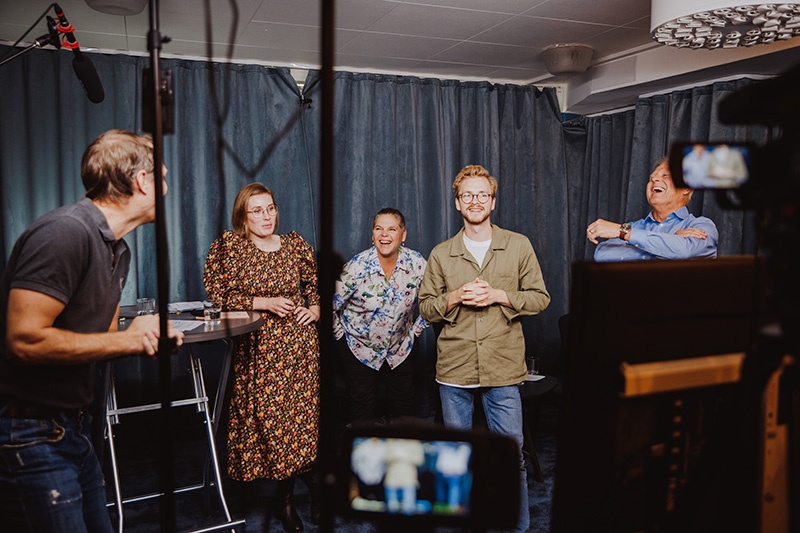 Fem personer står och samtalar glatt i en inspelningsstudio, foto.
